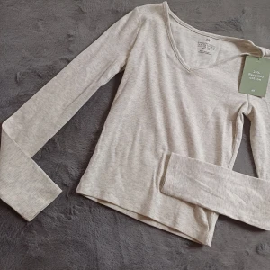 Beige ribbad tröja från H&M - Säljer en beige ribbad tröja från H&M i storlek 146/152. Tröjan är tillverkad av 25% återvunnen bomull och har en v-ringad design med långa ärmar. Perfekt för en stilren och bekväm look.