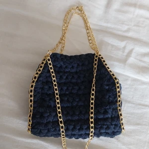 Mörkblå virkad väska med guldkedja - Snygg mörkblå virkad väska med elegant guldkedja. Perfekt för att ge din outfit en unik touch. Väskan har en mjuk och texturerad yta som ger en trendig look.