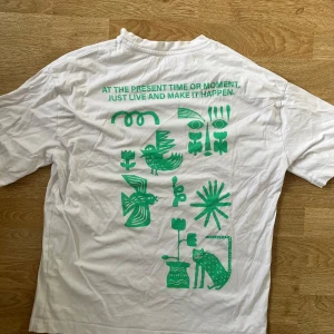 Vit t-shirt med grönt tryck - Säljer en vit t-shirt från Zara med ett unikt grönt tryck både fram och bak. Trycket inkluderar text och grafiska element som djur och växter. Perfekt för en avslappnad stil.
