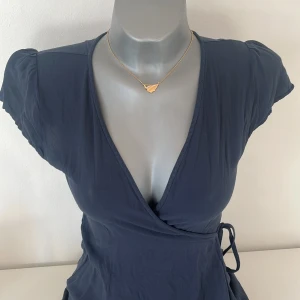 Mörkblå omlottklänning - Snygg mörkblå omlottklänning med korta ärmar och v-ringning. Klänningen har ett knytband i midjan för en justerbar passform. Perfekt för en stilren look.