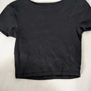 Svart ribbad kortärmad topp - Säljer en stilren svart ribbad topp med korta ärmar. Perfekt för en enkel och snygg look. Passar bra till både jeans och kjol.