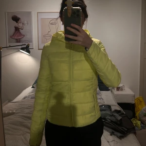 Gul pufferjacka med huva - Säljer en ljusgul pufferjacka med huva från Zara. Jackan har en dragkedja framtill och långa ärmar. Kommer passa en xss eller mindre xs