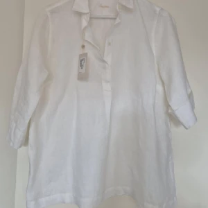 Vit linneblus från Stenströms - Säljer en elegant vit linneblus från Stenströms. Blusen har trekvartsärmar och en klassisk krage med knappar framtill. Perfekt för en stilren och luftig look. Går ej att förhandla, priset är fast