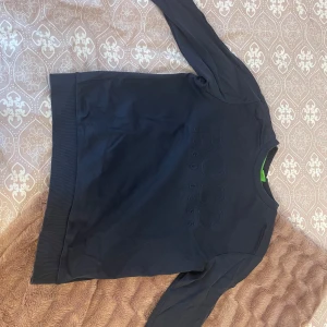 Svart tröja från Hugo Boss - Snygg svart tröja från Hugo Boss med broderad logga på framsidan. Tröjan har långa ärmar och ribbade muddar vid ärmslut och nederkant. Perfekt för en stilren look. Storlek L men passar för M 