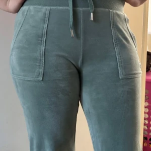Gröna mjukisbyxor från Juicy Couture - Snygga gröna mjukisbyxor från Juicy Couture med broderad logga. Byxorna har hög midja och praktiska fickor fram och bak. Perfekta för en avslappnad stil. Byxorna är endast använda ett par gånger.