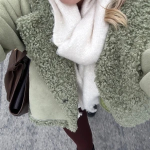 Grön teddyjacka från NA-KD - Säljer en snygg grön teddyjacka från NA-KD. Jackan har en mysig teddykrage och detaljer i samma material vid ärmslut och nederkant. Den stängs med knappar och har en normal passform. Perfekt för kyliga dagar! 🍃Saknar ett spänne