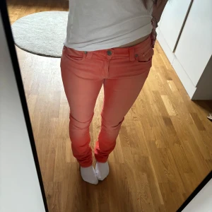 Korall jeans - Säljer ett par snygga korallrosa jeansbyxor med normal passform och låg midja. Byxorna har klassisk femficksdesign, bälteshällor och stängs med dragkedja och knapp. Perfekta för att liva upp din outfit! Storlek 34 (W25/W26) 