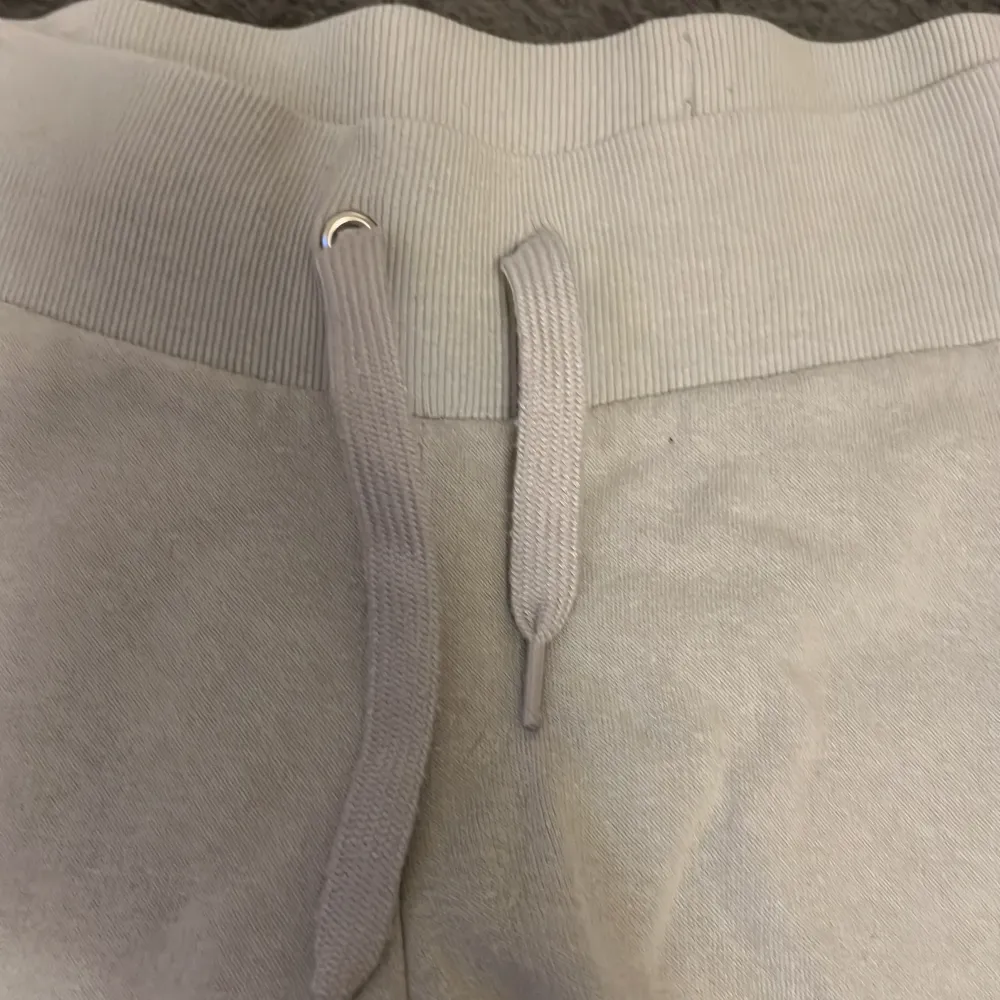 Säljer ett par ljusgrå mjukisbyxor från H&M med bred resår i midjan och dragsko. Byxorna har raka ben och är tillverkade i mjuk bomullsmix, perfekta för en avslappnad stil.. Farkut & Housut.