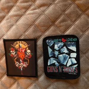 Guns N' Roses tygmärken - Två coola tygmärken med Guns N' Roses-motiv. Ena märket har bandets logga med rosor och dödskallar, det andra har texten 'Used to love her' och ett krossat glas-motiv. Perfekt att sy fast på jacka eller väska.