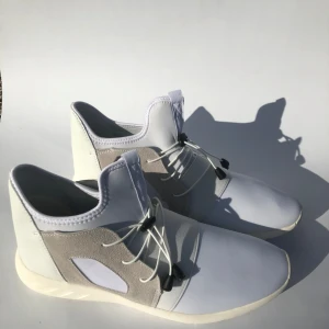 Vita och grå sneakers med snörning - Säljer ett par stilrena sneakers i vitt och ljusgrått med elastisk snörning och svarta detaljer. Skorna har en modern design med rund tå och paneler i syntetmaterial och mocka. Perfekta för dig som gillar minimalistisk stil. Storlek 44. Helt nya.