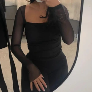 Svart långärmad topp - Snygg svart klänning med långärmade meshärmar och en tight passform. Perfekt för en elegant kvällslook. Klänningen har en stilren design med en fyrkantig urringning.