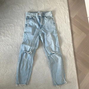 Ljusa jeans med slitningar - Snygga ljusa jeans med slitningar på knäna och fransiga benslut. Perfekta för en avslappnad stil. De har en klassisk femficksdesign och knappgylf.