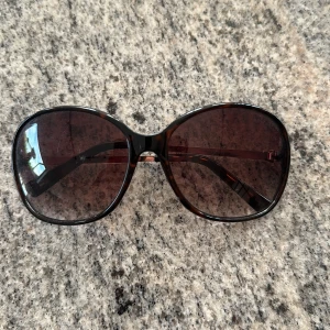 Bruna oversized solglasögon från Tommy Hilfiger - Stora, bruna solglasögon från Tommy Hilfiger med lätt tonade glas och sköldpaddsmönstrade bågar. Snygg metallogo på skalmarna och klassisk oversized form som ger en cool look.