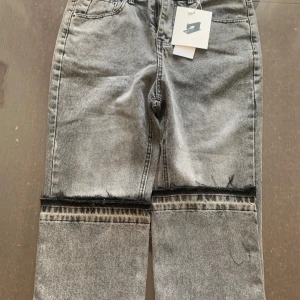 Grå washed flare jeans.  - Säljer ett par grå jeans med cool tvätt och råa, avklippta kanter vid knäna. Byxorna har dragkedja och knapp framtill samt klassiska fickor. Passformen är rak och de har en modern vibe.  Raka jeans Midja mått 40Cm och längd mått 105Cm. 