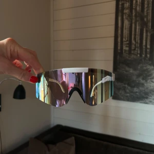 Sportiga solglasögon med spegelglas - Snygga sportiga solglasögon med spegelglas och vit båge. Perfekta för en aktiv livsstil med en modern look. Glasögonen har en omslutande design som ger bra skydd mot solen.