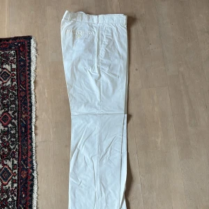 Vita byxor från Pat Nickol's - Snygga vita byxor från Pat Nickol's med en klassisk design. Byxorna har en knappdetalj vid bakfickan och är perfekta för en stilren look. De är tillverkade i ett lätt och bekvämt material.