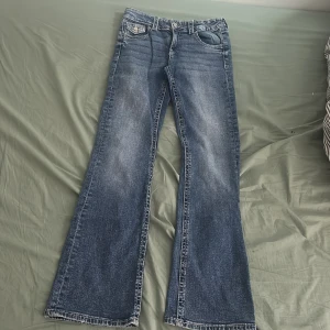 Blå bootcut jeans från Gina Tricot - Snygga blå bootcut jeans från Gina Tricot med dekorativa bakfickor. Perfekta för en avslappnad stil. Klassisk femficksdesign och knappgylf.