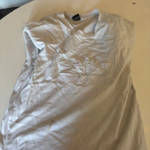 Vit t-shirt från GANT - Säljer en vit t-shirt från GANT med broderad logga på framsidan. T-shirten är kortärmad och har en klassisk rund halsringning. Perfekt för en avslappnad stil.