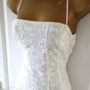 Vit broderad kortklänning med smala axelband - Superfin vit klänning med smala axelband och broderade blommor. Klänningen har en figurnära passform upptill och utställd kjol, perfekt för sommarens alla tillfällen. Söt och fräsch stil med romantiska detaljer. Perfekt till studenten! 