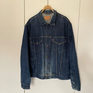 Levi's Jeansjacka - Säljer en klassisk blå jeansjacka från Levi's med knappar framtill och två bröstfickor med lock. Jackan har en normal passform och är perfekt för vår och höst. Den har långa ärmar och en stilren design som aldrig går ur tiden.                          Mått: Krage till öppning 70 cm Armhåla t armhåla 65 cm Ärm längd 69 cm