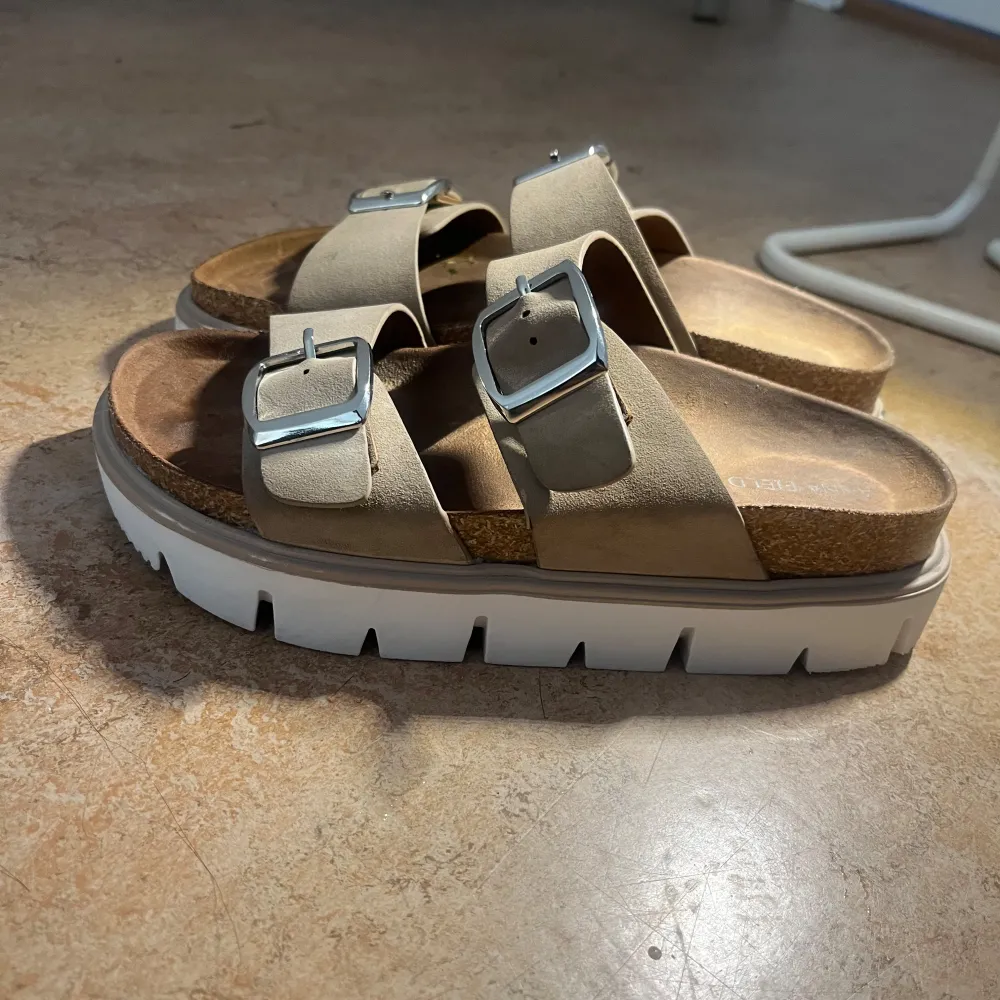 Säljer ett par snygga beige sandaler från Anna Field med dubbla remmar och silverfärgade spännen. Sandalerna har en bekväm korksula och en vit, tjock plattformssula som ger extra höjd och stil.. Kengät.