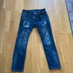Blå jeans från Dsquared2 - Snygga blå jeans från Dsquared2 med slitna detaljer och färgstänk för en trendig look. De har en klassisk femficksdesign och knappgylf. Perfekta för dig som vill ha en unik stil. Storle 48 passar som S/M