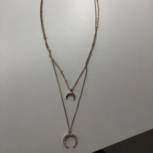 Guldigt halsband med månhänge - ❗️SKRIV T MIG VID KÖP ❗️Dubbelkedjat guldigt halsband med två månhängen. Det ena hänget är dekorerat med glittrande stenar, medan det andra är enkelt och stilrent. 
