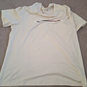 Beige t-shirt med tryck - Säljer en beige t-shirt med ett stilrent tryck i svart och rött på bröstet. T-shirten har korta ärmar och är perfekt för en avslappnad stil. Passar bra till jeans eller shorts.