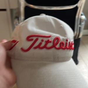 Vit keps från Titleist med röd brodyr - Säljer en vit keps från Titleist med tydlig röd broderad logga framtill. Klassisk böjd skärm och justerbar passform baktill. Perfekt för golf eller andra utomhusaktiviteter.