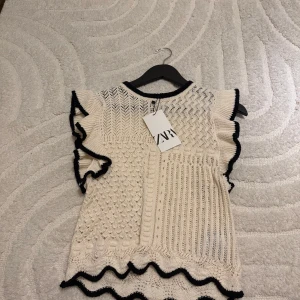 Vit stickad topp från Zara - Säljer en helt ny vit stickad topp från Zara med svarta kanter och volangdetaljer💗