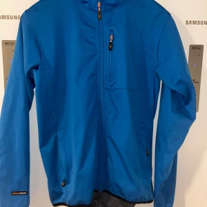 jacka från Pinewoodstl S - Säljer en blå jacka från Pinewood med dragkedja och långärmade ärmar. Jackan har en praktisk bröstficka och en snygg logga på ärmen. Perfekt för utomhusaktiviteter!