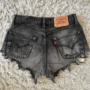 Svarta/grå jeansshorts från Levi's - Säljer ett par svarta/grå jeansshorts från Levi's. Shortsen har slitna detaljer för en cool vintage-look. Perfekta för sommaren! Oklar vad för storlek men tror runt s/m. Passar mig som vanligtvis har S. 