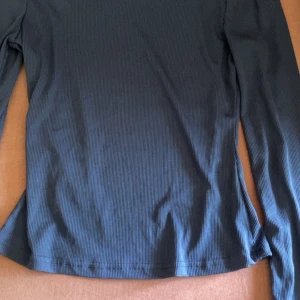 Marinblå långärmad topp - Säljer en trendig marinblå långärmad tajt topp. Perfekt att matcha med jeans eller kjol för en avslappnad look. Tunn och mjuk i materialet, sitter skönt mot kroppen.