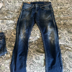 Blå jeans från Dondup - Säljer ett par snygga blå jeans från Dondup med slitna detaljer och en klassisk femficksdesign. Jeansen har en normal passform och är tillverkade i denim med en lätt tvättad look. Perfekta för en avslappnad stil. 