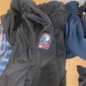 Svart jacka från PJS - Säljer en svart jacka från PJS med ett snyggt märke på ärmen. Jackan har en stilren design och är perfekt för kyligare väder. Den är tillverkad i ett slitstarkt material och har en bekväm passform.