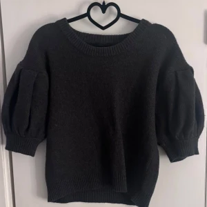 Mörkgrå stickad tröja från Lindex - Mysig mörkgrå stickad tröja från Lindex med puffiga trekvartsärmar och bred ribbad kant vid hals, ärmslut och nederkant. Knappt använd, inga skador eller knoppar på tröjan.