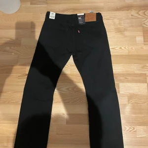Svarta Levis 501 jeans - Säljer ett par klassiska svarta Levis 501 jeans som är helt nya. De har en rak passform och är tillverkade i slitstarkt denim. Perfekta för en stilren look. Jeansens ikoniska design gör dem tidlösa och mångsidiga. Storlek L32 och W32!