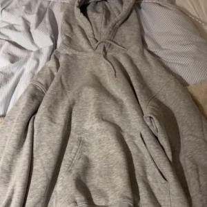 Grå hoodie - Säljer en klassisk grå hoodie med känguruficka och justerbar huva. Perfekt för en avslappnad stil och passar till det mesta. Skön och enkel att bära.
