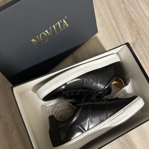 Svarta sneakers från Novita - Snygga svarta sneakers från Novita i skinn med vit sula. Skorna har en stilren design med snörning och en diskret logga på sidan. Perfekta för en casual look. Helt nya! 