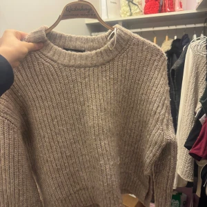 Beige stickad tröja från Gina Tricot - Mysig beige stickad tröja från Gina Tricot. Perfekt för kyliga dagar med sin varma och bekväma design. Tröjan har en rund hals och långa ärmar, vilket gör den idealisk för både höst och vinter. Använd endast en gång på en konsert. 