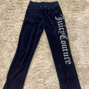 Mörkblå velourbyxor från Juicy Couture - Snygga mörkblå velourbyxor från Juicy Couture med glittrig logga längs benet. Byxorna är låga i midjan och har praktiska fickor. Perfekta för en avslappnad och stilren look. Det står ingen storlek i men skulle säga XXS/XS.💞Petite 