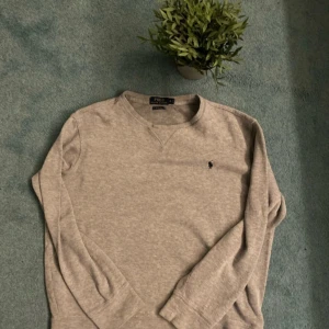 Grå tröja från Polo Ralph Lauren - Säljer en stilren grå tröja från Polo Ralph Lauren med det klassiska broderade logotypen på bröstet. Tröjan har långa ärmar och en rund halsringning. Perfekt för en avslappnad och snygg look.