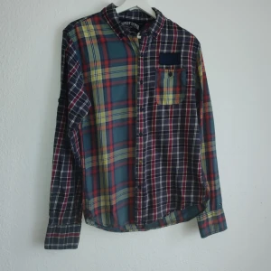 Rutig skjorta från Hilfiger Denim - Snygg rutig skjorta från Hilfiger Denim i flera färger som blå, röd och gul. Skjortan har långa ärmar och en klassisk krage. Den är försedd med knappar framtill och en bröstficka med en diskret logga ovanför. Perfekt för en avslappnad stil.