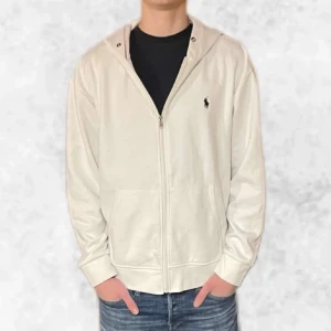 Vit zip hoodie från Ralph Lauren  - Säljer en stilren vit zip hoodie från Ralph Lauren. Den är i väldigt fint skick förutom att den är lite nopprig men det syns knappt vid använding. Den är i storlek L men är liten i storleken så passar snarare M. Personen på bilden är 183 cm. Vid frågor eller funderingar är det bara att höra av sig.