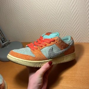 Nike Sb dunk low  - Säljer ett par Nike Dunk med en unik färgkombination av turkos och orange. Skorna är tillverkade i mocka och har en klassisk Nike-logga på sidan. De har turkosa detaljer och orange snörning som ger en cool kontrast. Lite använda men inte särskilt slitna.