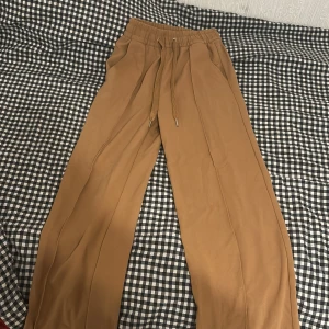 Bruna byxor från H&M - Snygga bruna byxor från H&M med elastisk midja och dragsko för en bekväm passform. Byxorna har en avslappnad stil och är perfekta för en casual look. Tillverkade i ett mjukt material som ger en skön känsla hela dagen.