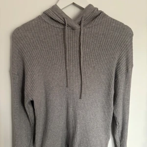 Grå stickad hoodie - Säljer en stilren grå ribbstickad hoodie med långa ärmar och huva. Perfekt för en avslappnad look. Passar bra till både jeans och mjukisbyxor.