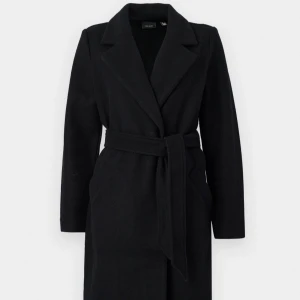 Svart kappa från Vero Moda - Elegant svart kappa från Vero Moda med knytbälte i midjan. Den har en klassisk krage och långa ärmar, perfekt för kyligare dagar. Stilren och tidlös design som passar till många tillfällen! 💕Ps den är nopprig på ärmarna!