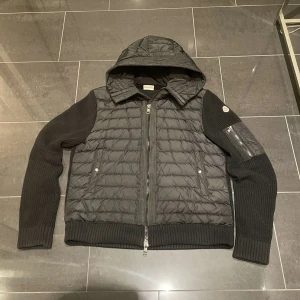 Svart jacka från Moncler - Snygg svart jacka från Moncler med quiltad design och huva. Jackan har långa ärmar och dragkedja framtill. Perfekt för kyligare dagar med sin stilrena look och praktiska fickor. Skicka 9/10