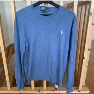 Blå tröja från Polo Ralph Lauren - Säljer en stilren blå tröja från Polo Ralph Lauren i slim fit. Tröjan har långa ärmar och ett litet gult broderat märke på bröstet. Perfekt för en avslappnad men ändå elegant look.